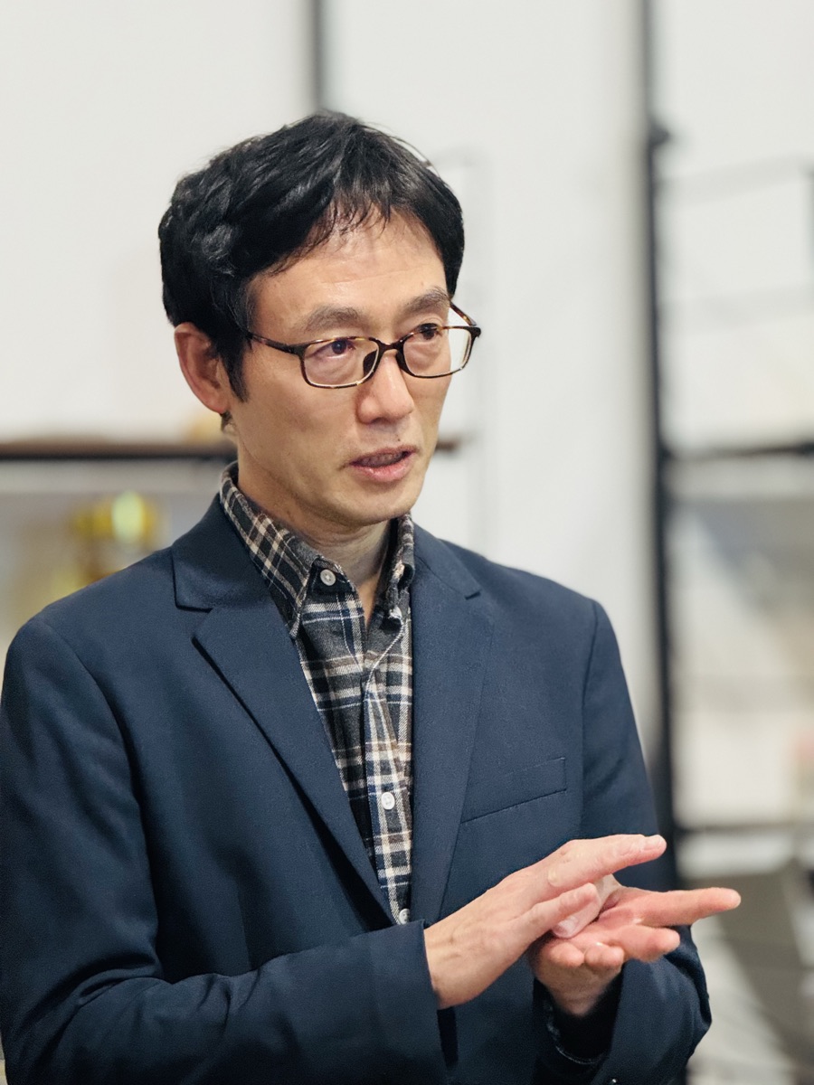 山口竜さん。眼鏡をかけ、紺のジャケット姿で話しているところ。